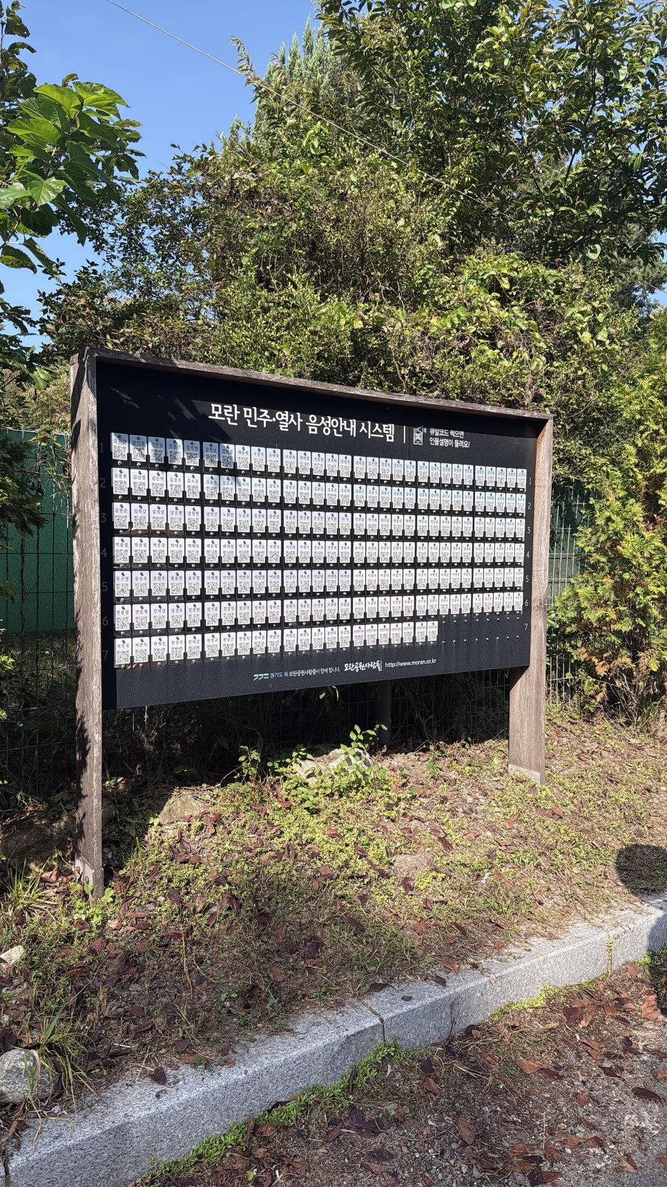 역사를 바꾼 것은 초인이 아니었습니다 — 모란공원 입구의 민주열사 음성안내 시스템 안내판, QR 명패가 빼곡하다